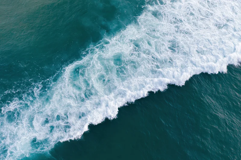Aerial top-down view of ocean waves breaking in a diagonal line with white foam on turquoise water