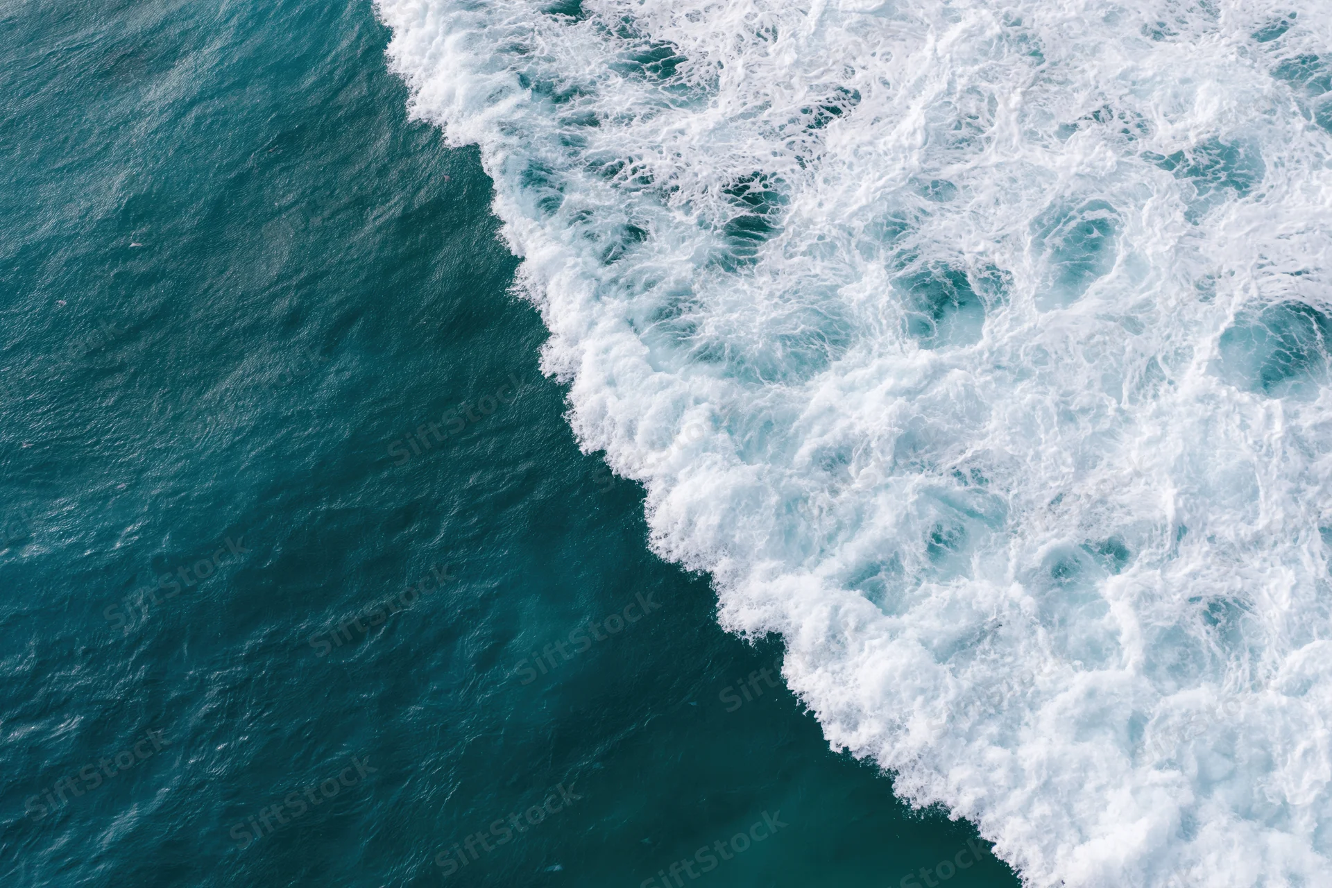 Aerial top-down view of ocean waves breaking along a diagonal line with white foam and deep blue water