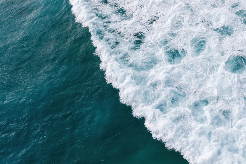 Aerial top-down view of ocean waves breaking along a diagonal line with white foam and deep blue water