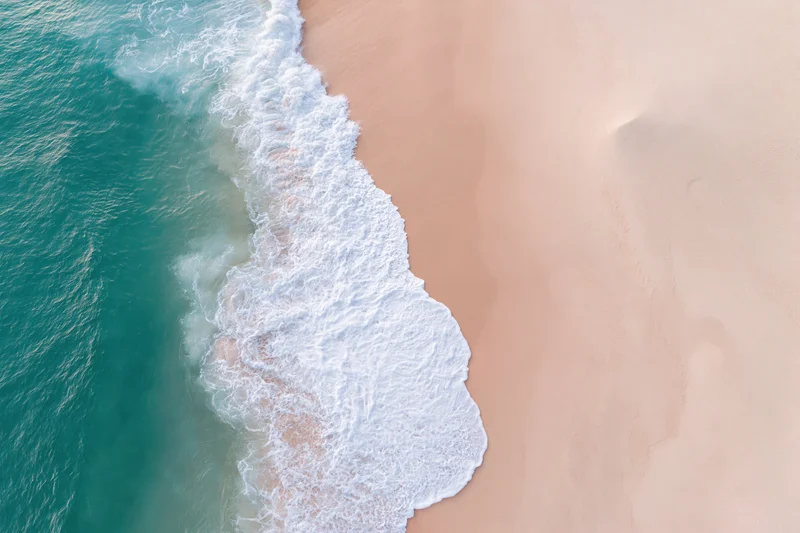 Aerial top-down view of ocean waves meeting a wide sandy beach
