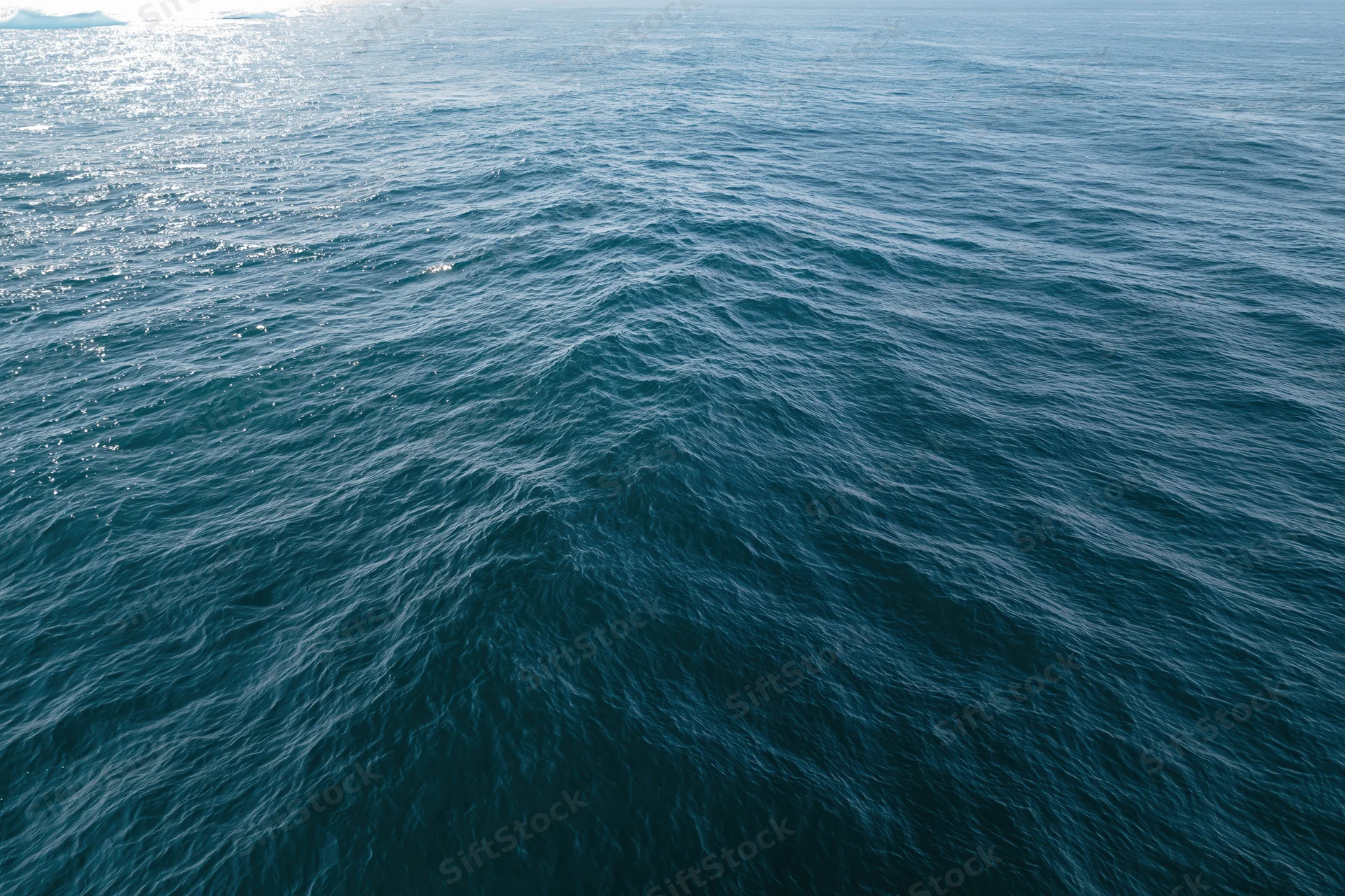 Aerial top-down view of open ocean surface with gentle ripple and sunlight reflection