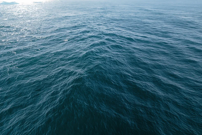 Aerial top-down view of open ocean surface with gentle ripple and sunlight reflection