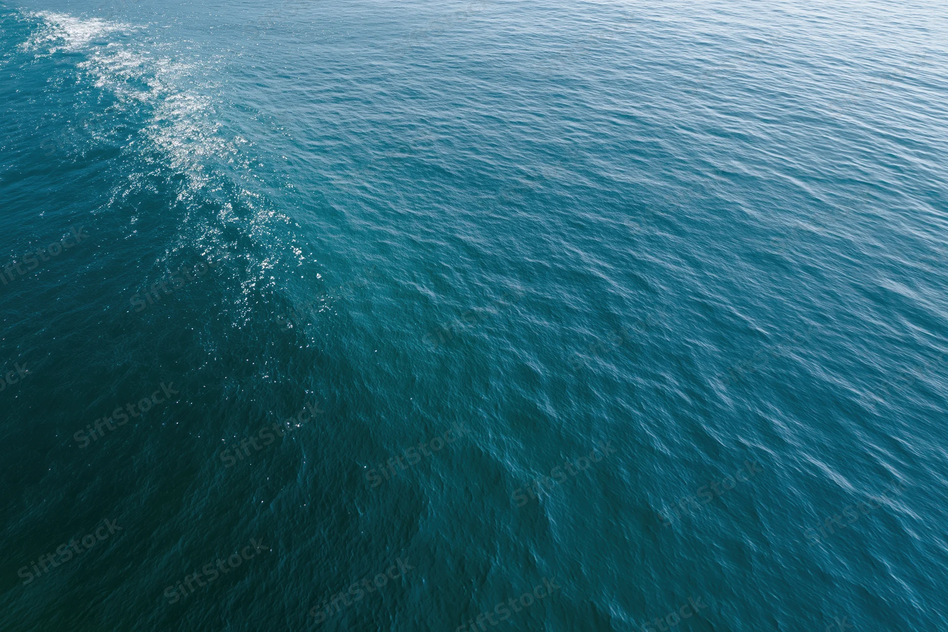 Aerial top-down view of open ocean surface with gentle ripple and sunlight reflection