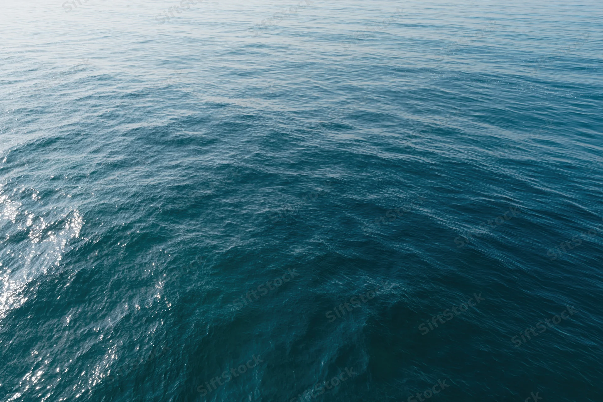 Aerial top-down view of open ocean surface with gentle ripples and sunlight reflections