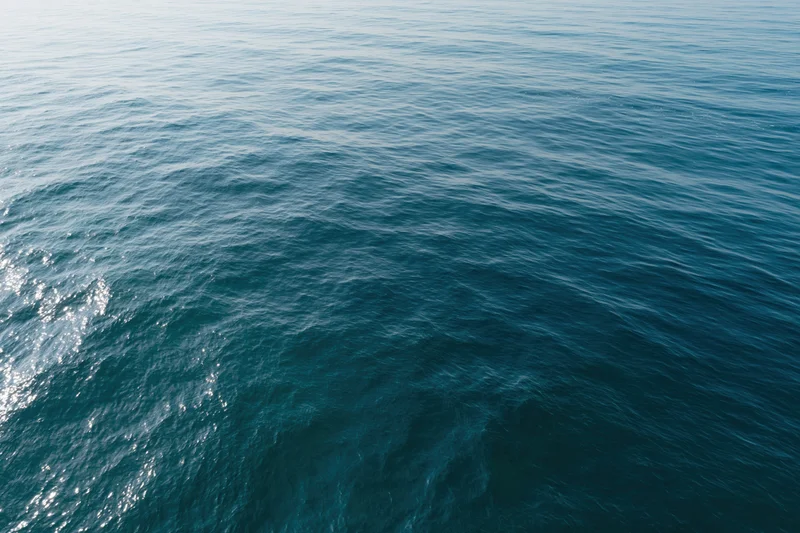 Aerial top-down view of open ocean surface with gentle ripples and sunlight reflections