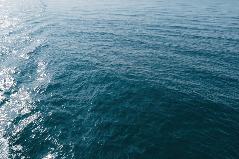 Aerial top-down view of open ocean surface with gentle ripples and sunlight reflections