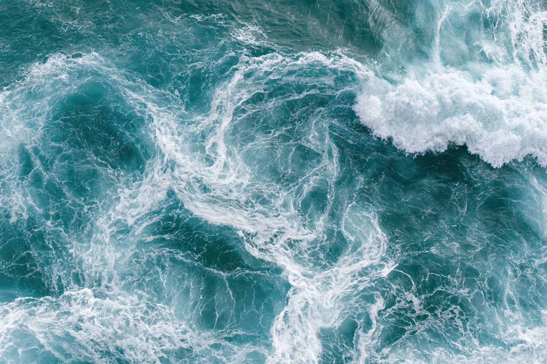 Aerial top-down view of turbulent ocean waves with white foam and swirling currents