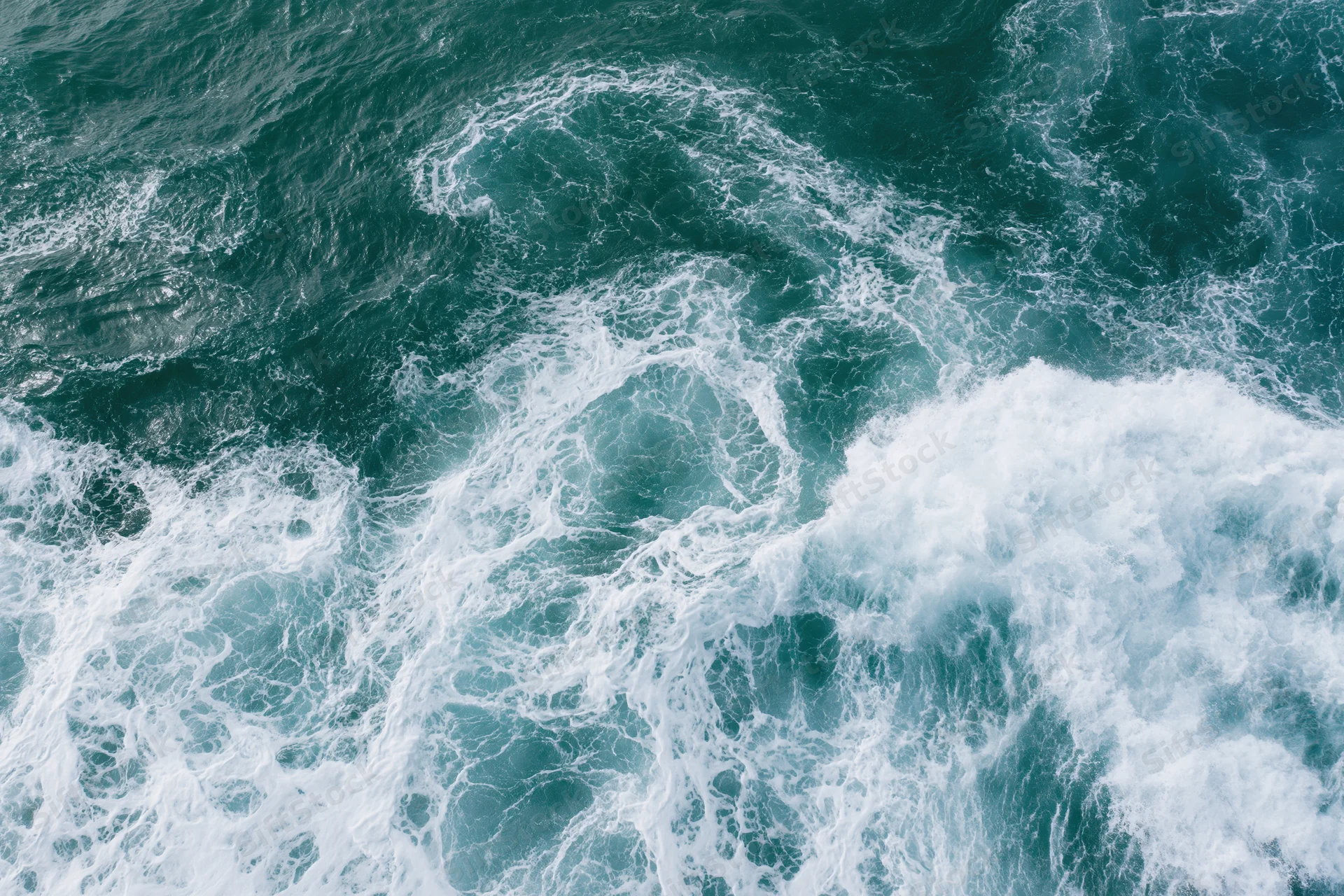 Aerial top-down view of turbulent ocean waves with white foam and swirling currents