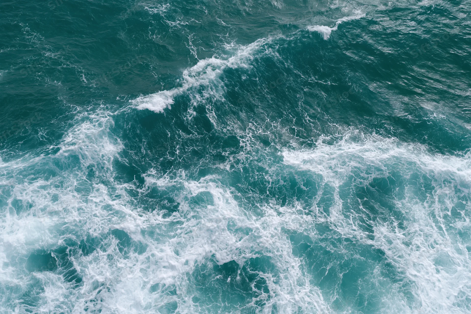 Aerial top-down view of turbulent ocean waves with white foam and turquoise water
