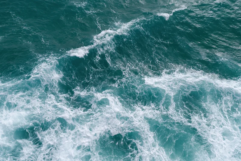 Aerial top-down view of turbulent ocean waves with white foam and turquoise water