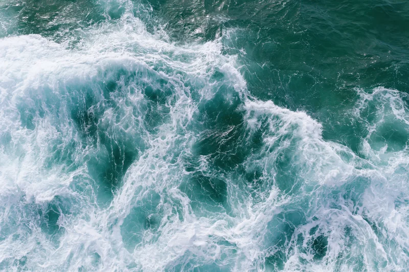 Aerial top-down view of turbulent ocean waves with white foam and turquoise water