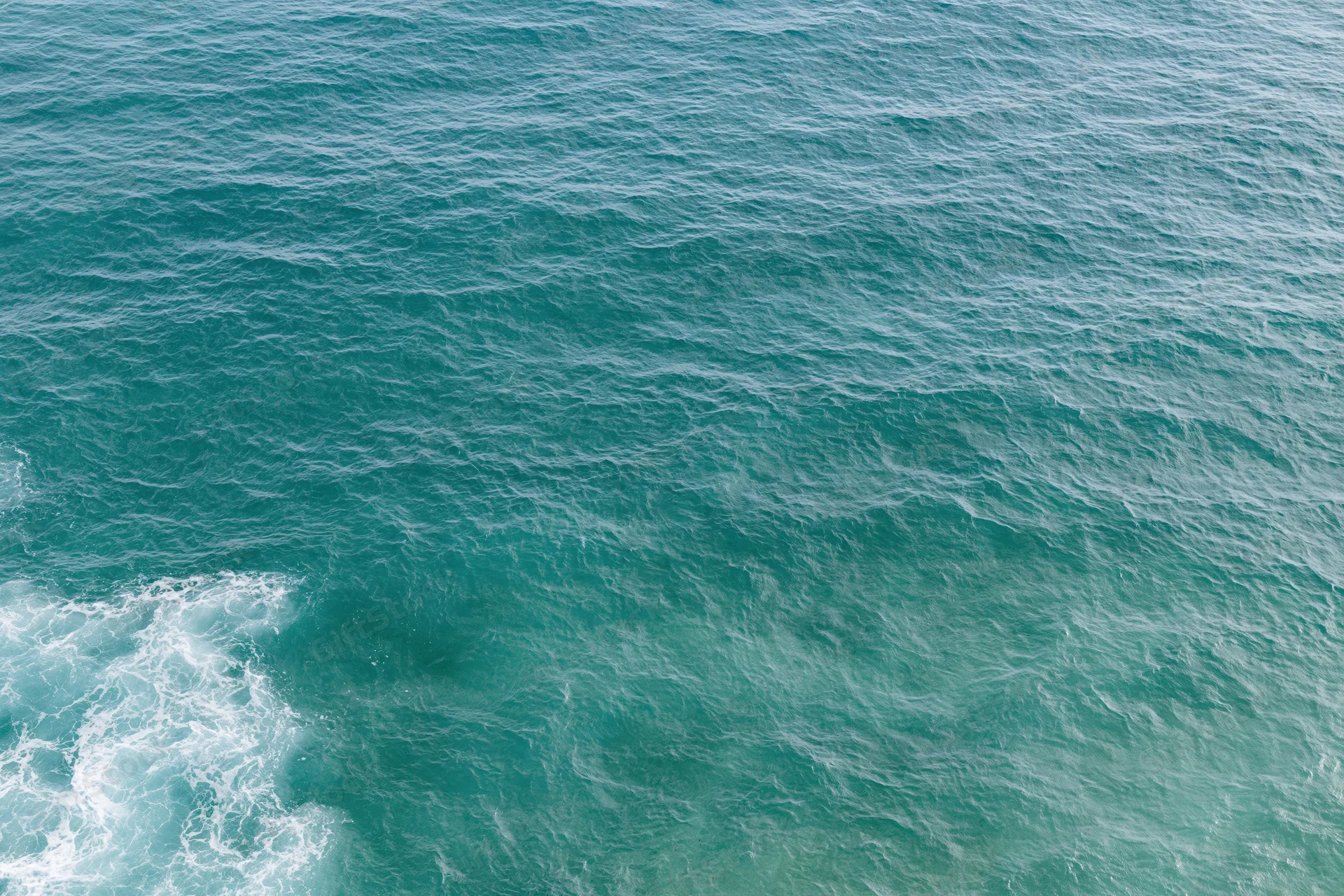 Aerial top-down view of open ocean surface with small wind-rippled waves and white foam