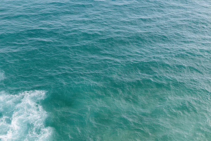 Aerial top-down view of open ocean surface with small wind-rippled waves and white foam