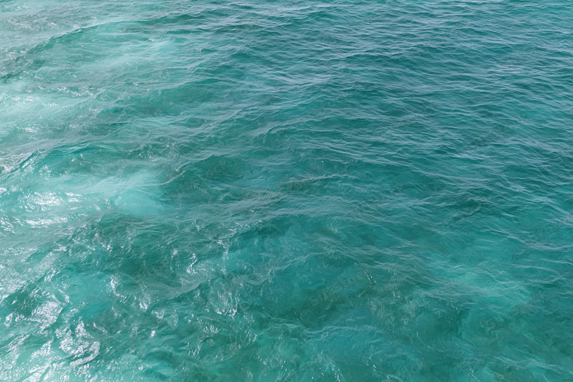 Aerial top-down view of open ocean surface with small wind-rippled waves and turquoise water