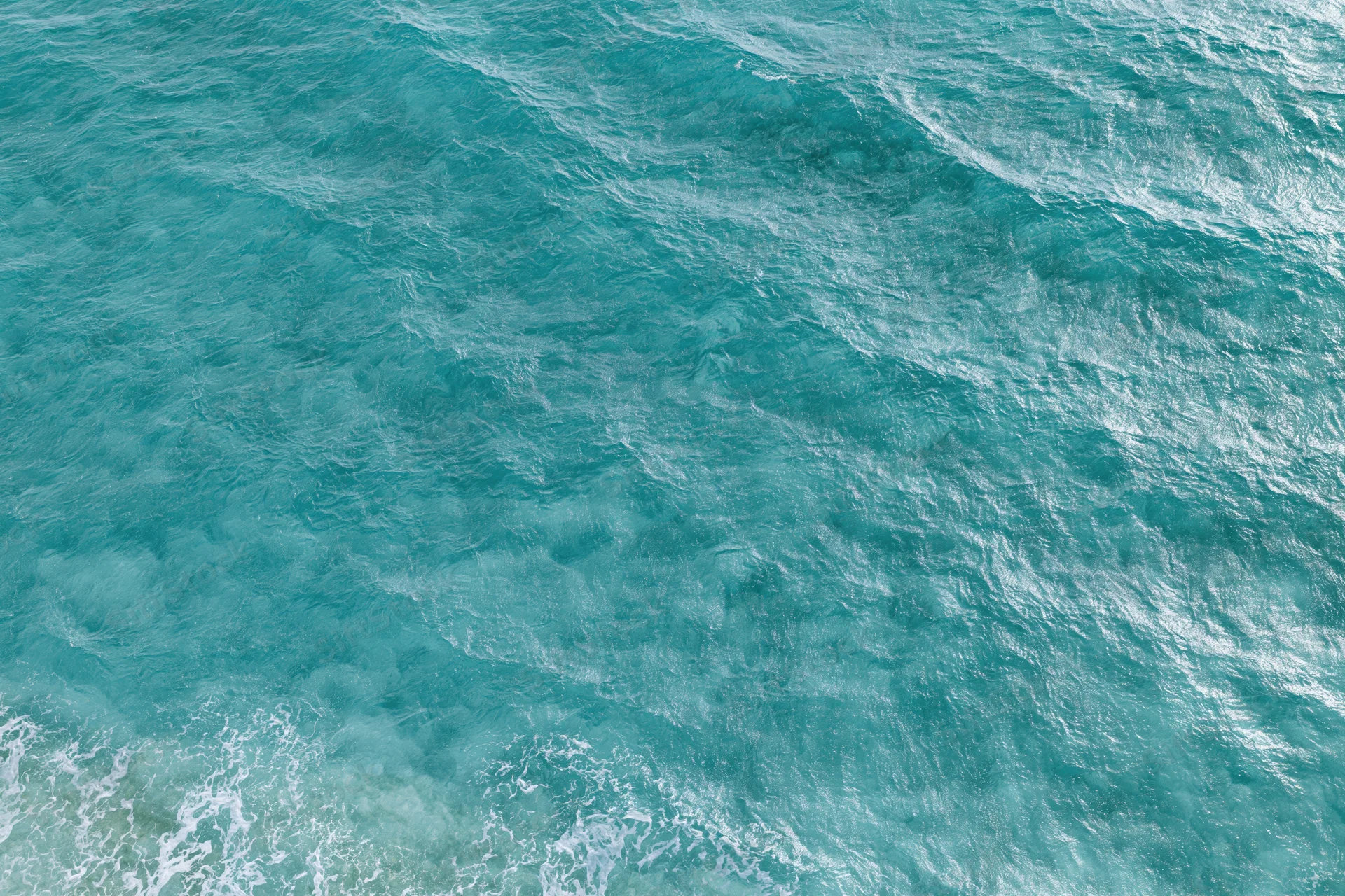 Aerial top-down view of rippling ocean surface with small waves and white foam