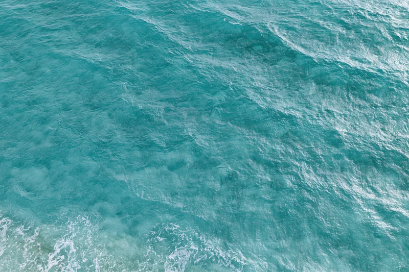 Aerial top-down view of rippling ocean surface with small waves and white foam