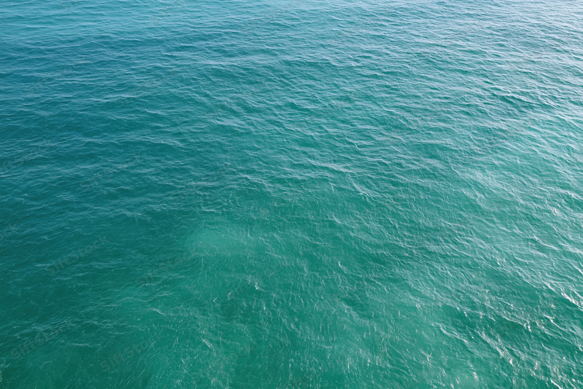 Aerial top-down view of calm turquoise ocean surface with small ripples and waves