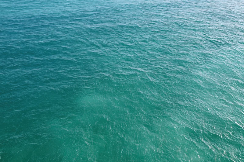 Aerial top-down view of calm turquoise ocean surface with small ripples and waves