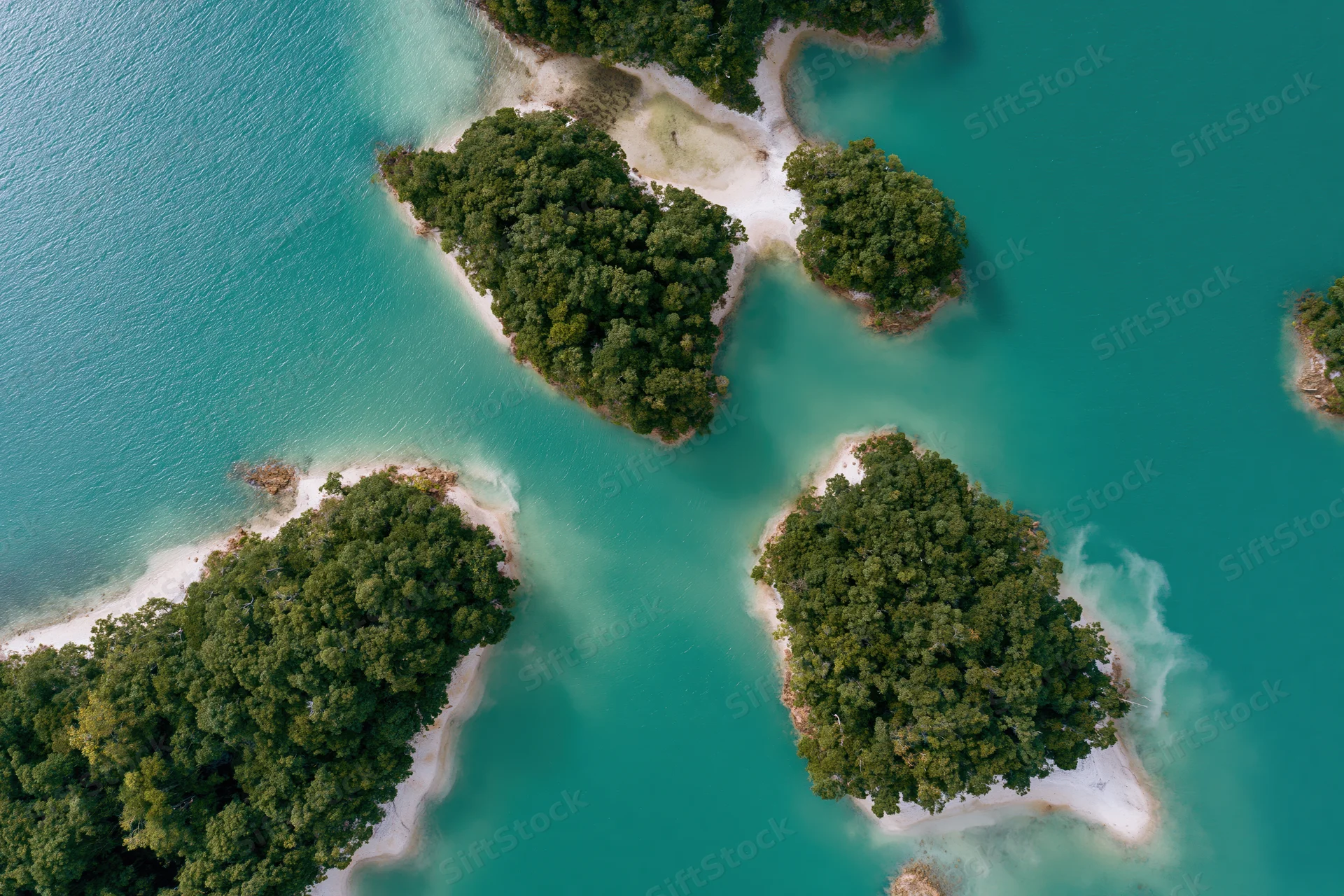 Aerial top-down view of scattered small forested islands in turquoise water