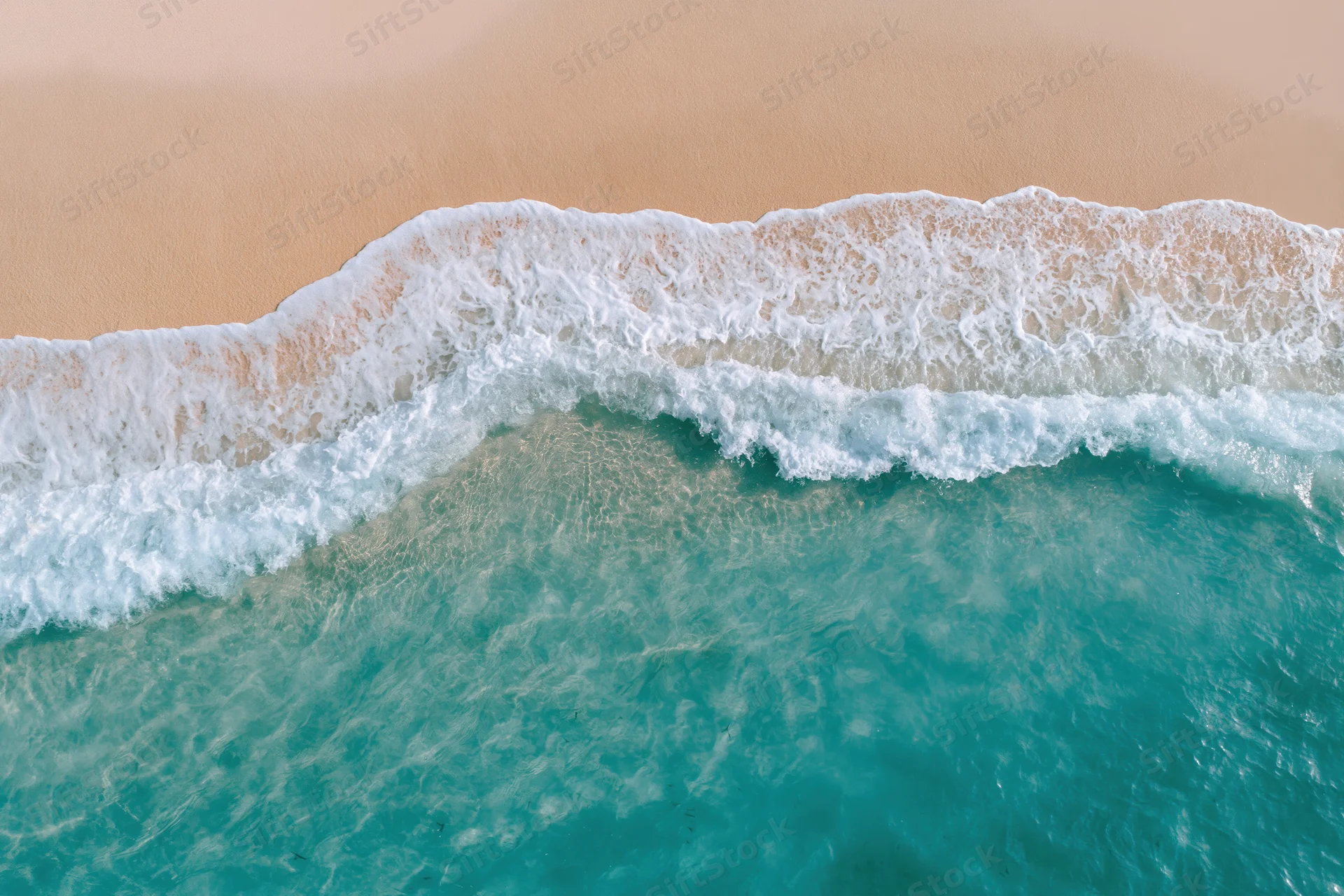 Aerial top-down view of turquoise ocean waves meeting sandy beach