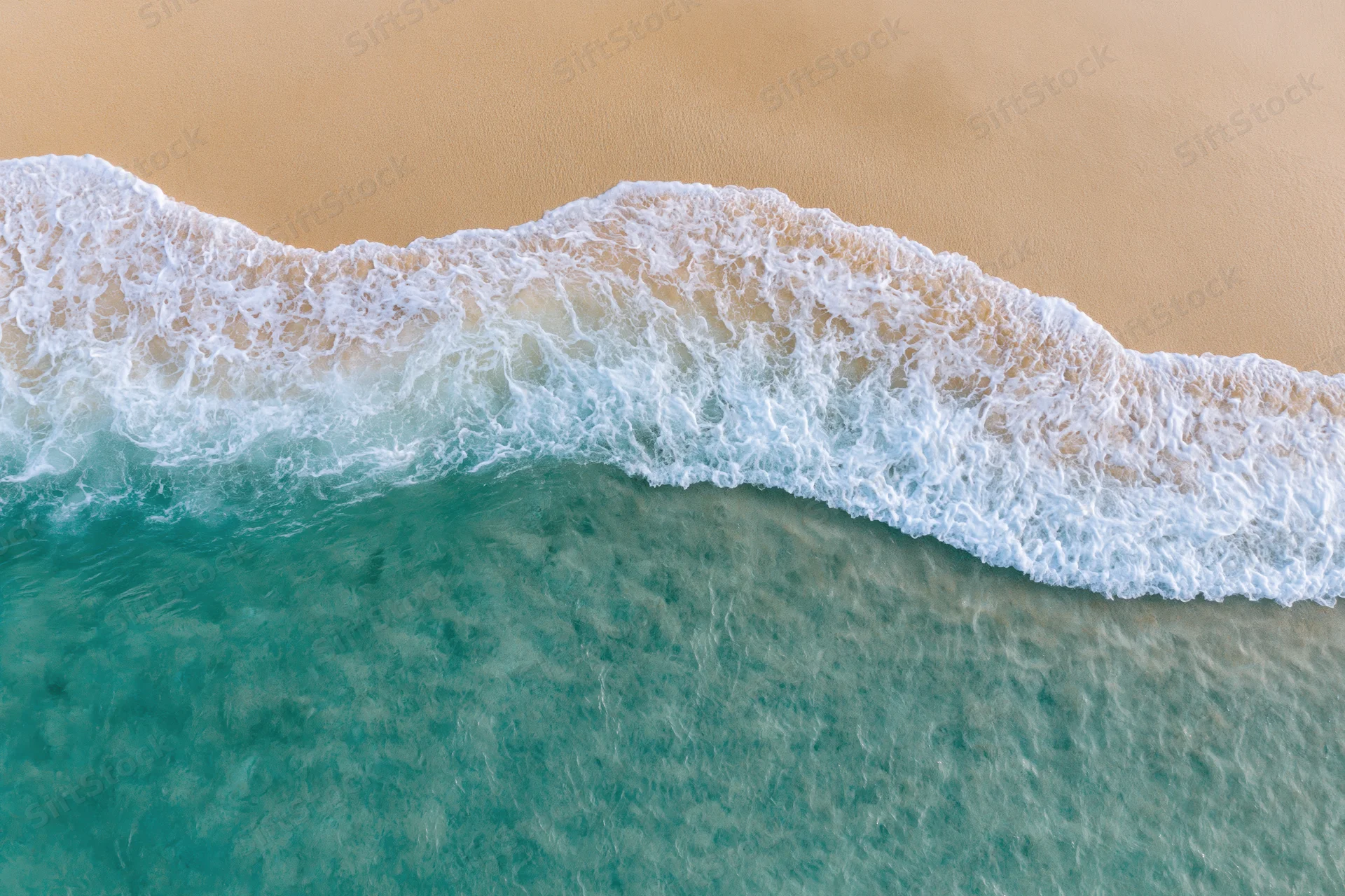 Aerial top-down view of turquoise ocean waves meeting sandy beach