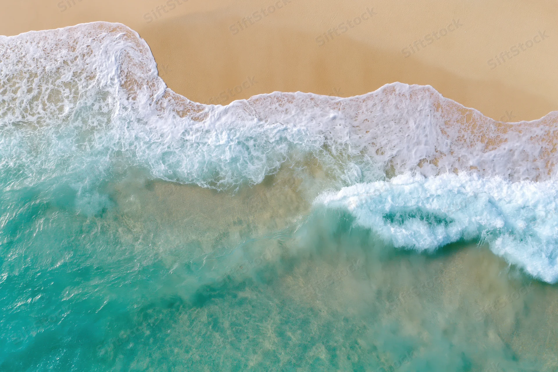 Aerial top-down view of turquoise ocean waves gently breaking on sandy beach