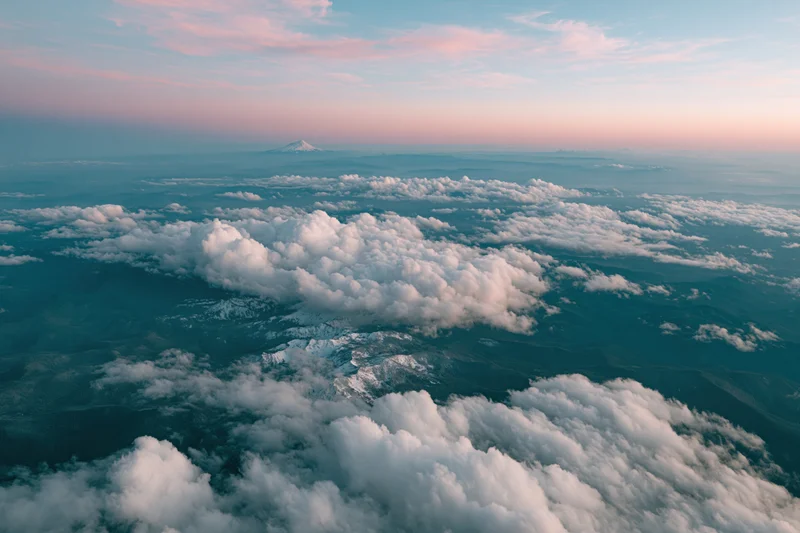 Aerial view from airplane window looking down at snow-capped mountain and clouds at twilight