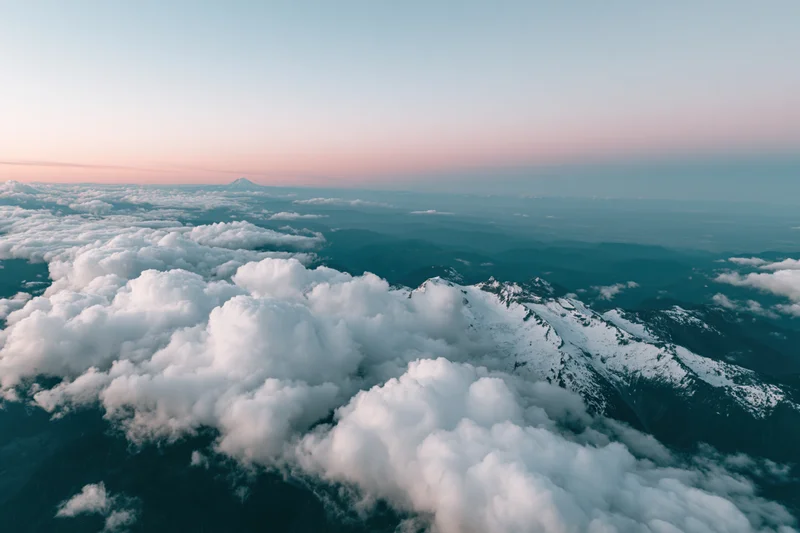 Aerial view of snow-capped mountains and clouds from airplane window at dusk
