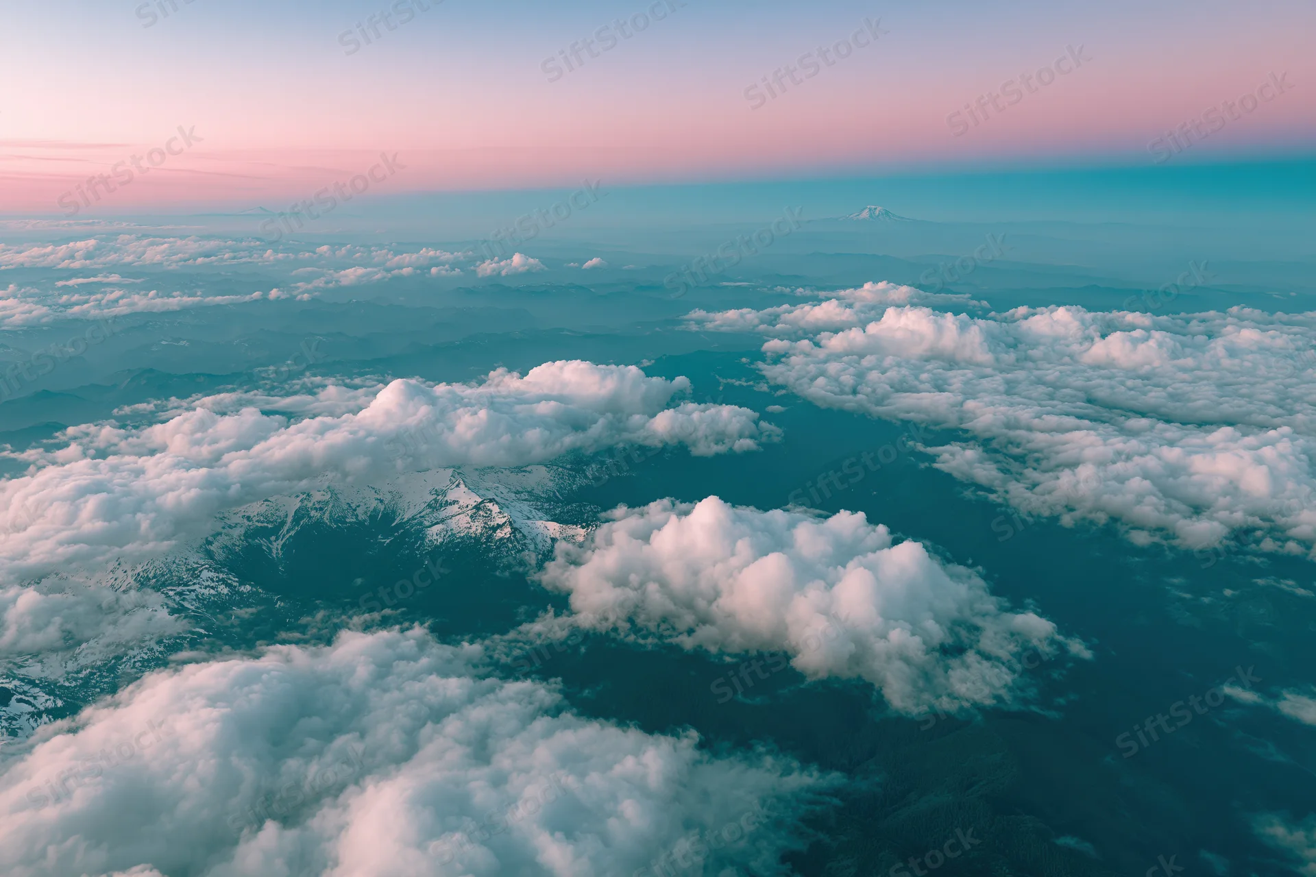 Aerial view from airplane window looking down at snow-capped mountains and clouds at twilight