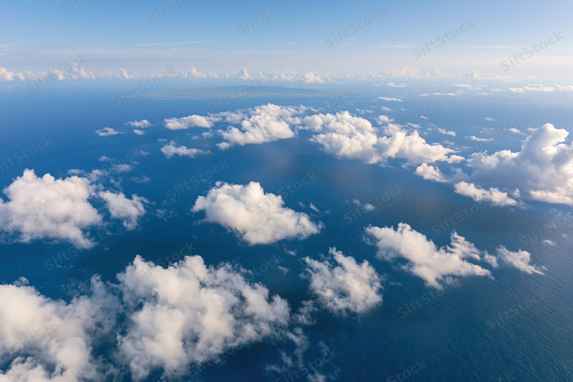 Aerial view of ocean and clouds from above with distant island on horizon