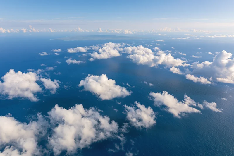 Aerial view of ocean and clouds from above with distant island on horizon