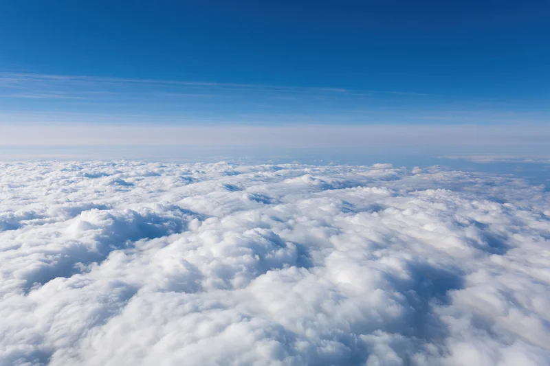 Aerial view of dense white cumulus clouds below a clear blue sky