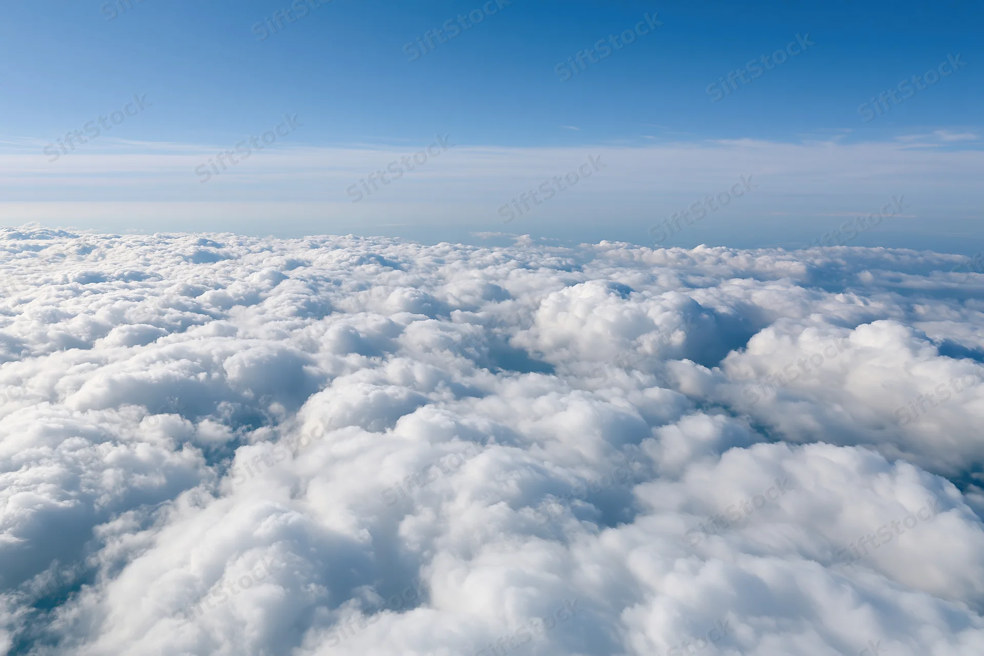 Aerial view of dense white cumulus clouds stretching across the sky below a clear blue expanse