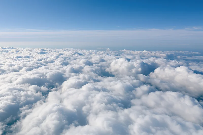 Aerial view of dense white cumulus clouds stretching across the sky below a clear blue expanse