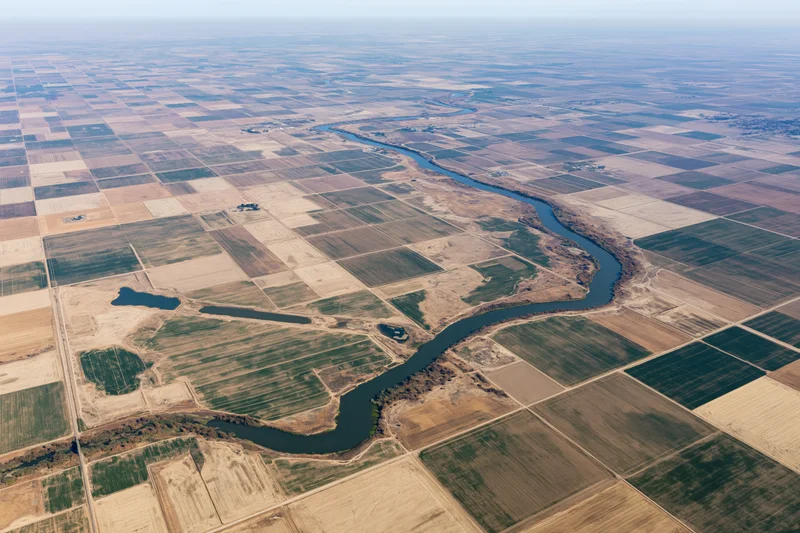 Aerial view of a winding river cutting through a vast grid of agricultural fields