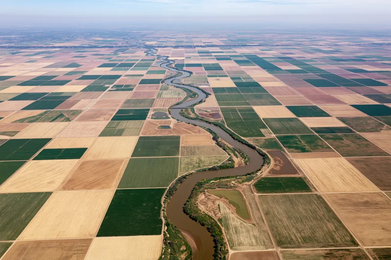 Aerial view of a winding river cutting through a vast patchwork of cultivated agricultural fields