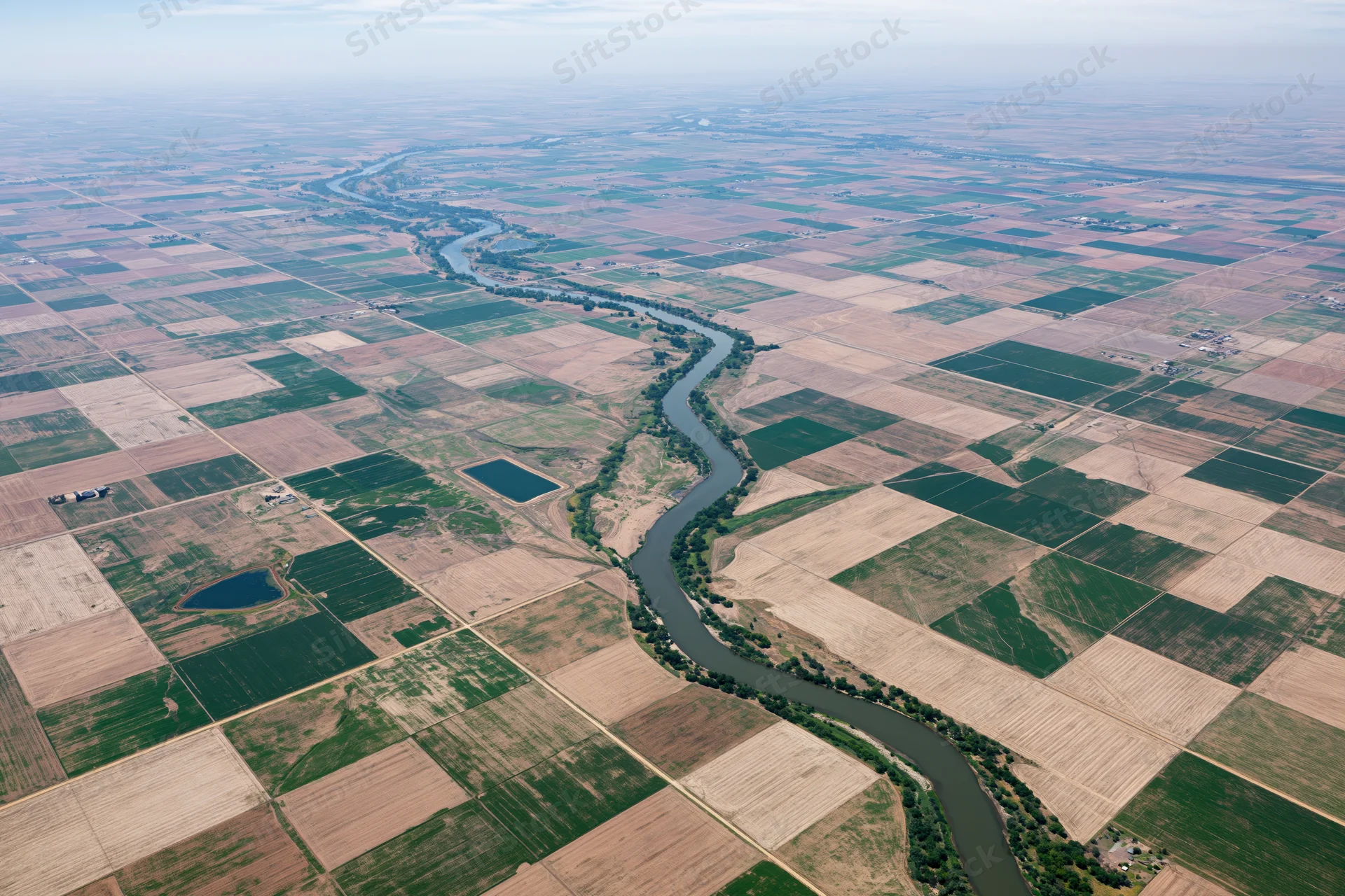 Winding river cutting through a grid of cultivated agricultural fields from above