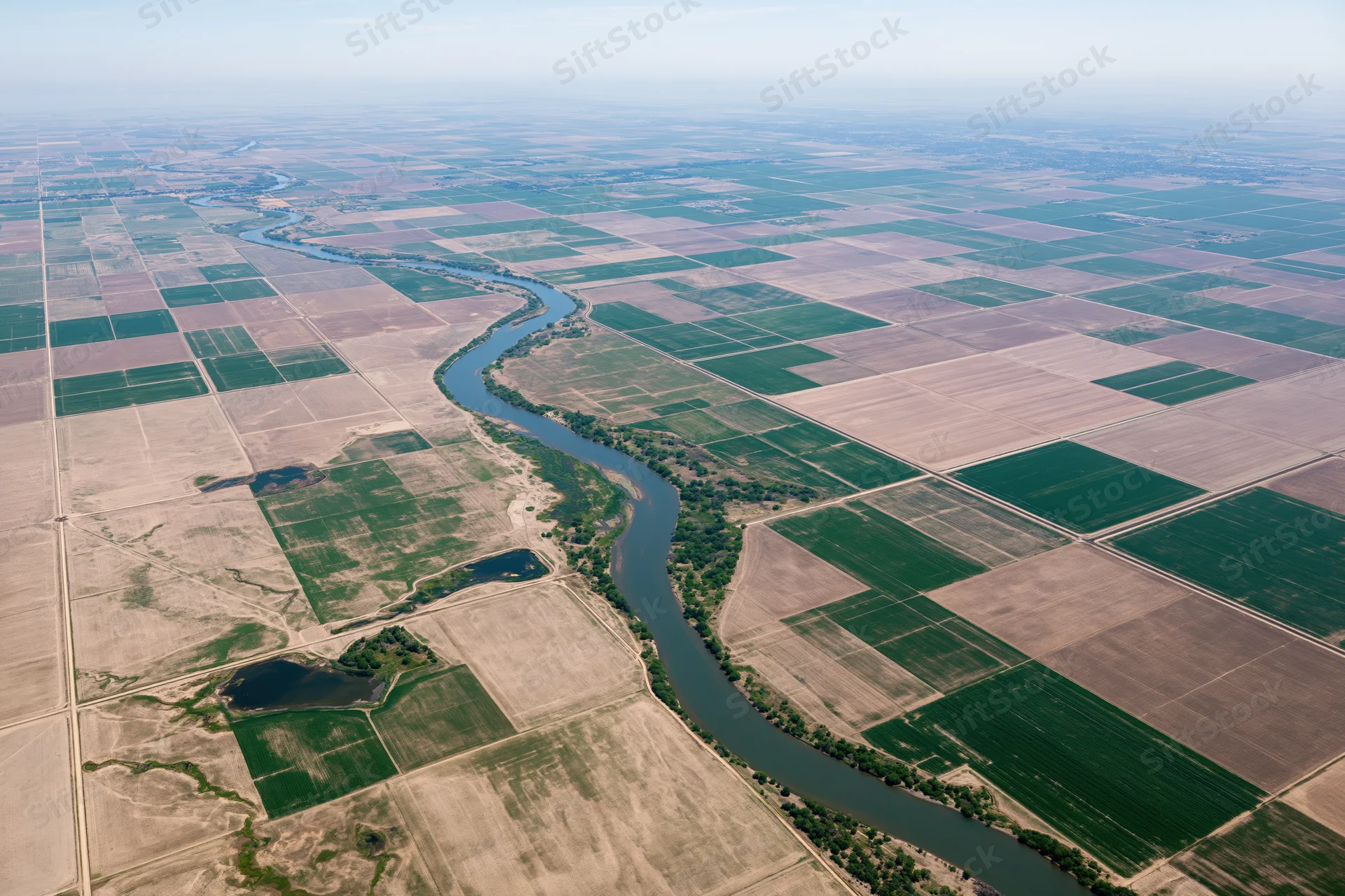 Aerial view of a winding river cutting through a vast grid of cultivated agricultural fields