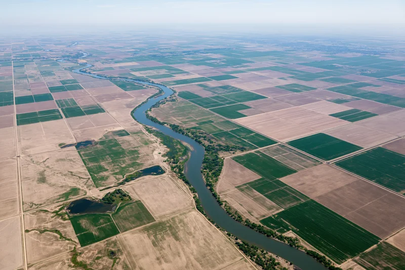 Aerial view of a winding river cutting through a vast grid of cultivated agricultural fields