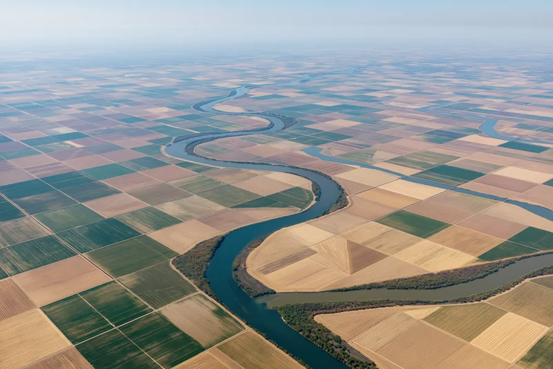 Winding river flowing through a patchwork of cultivated agricultural fields from above