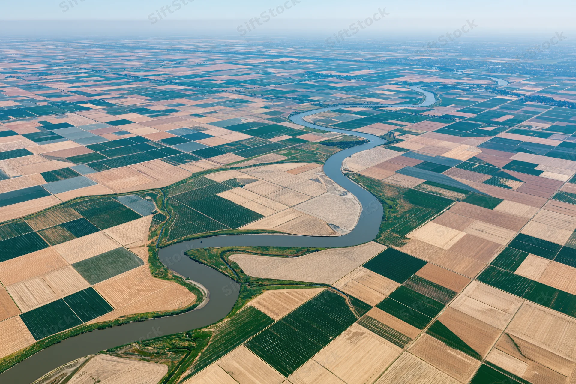 Aerial view of a winding river cutting through a patchwork of cultivated farmland fields