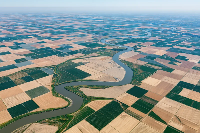 Aerial view of a winding river cutting through a patchwork of cultivated farmland fields