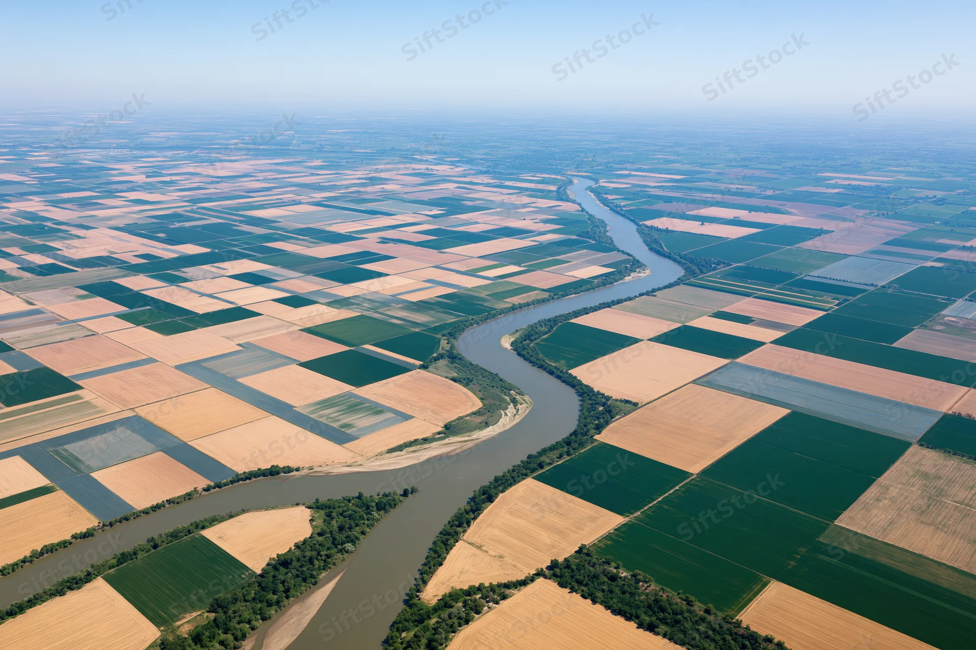 Aerial view of a winding river cutting through patchwork farmland under clear sky