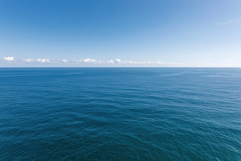 Aerial view of calm ocean stretching to horizon under clear blue sky