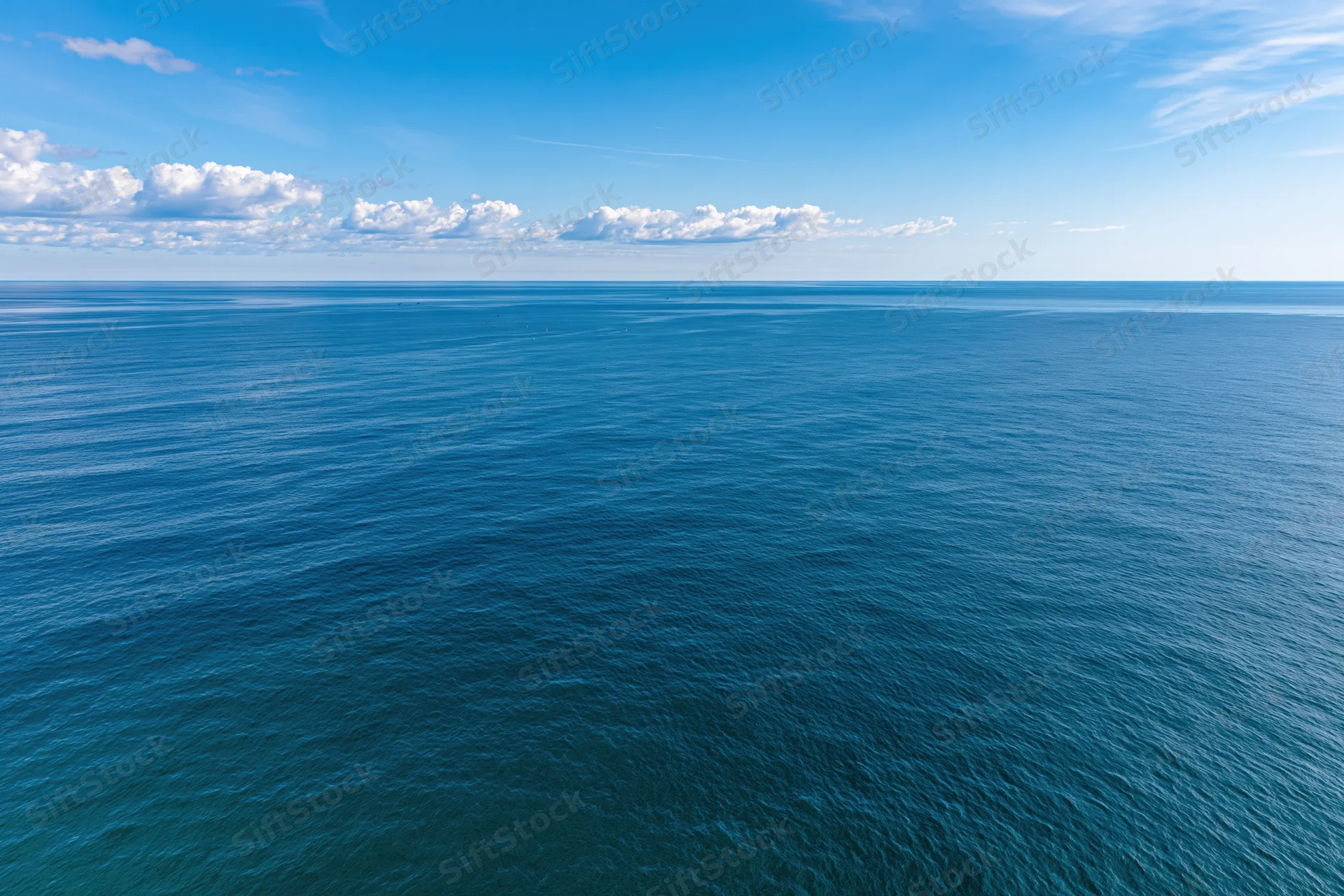 Aerial view of calm ocean stretching to horizon under blue sky with scattered clouds