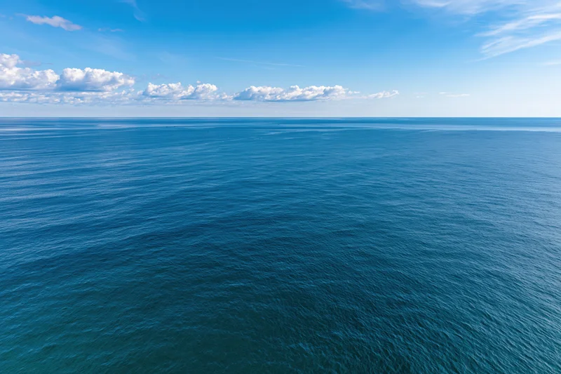 Aerial view of calm ocean stretching to horizon under blue sky with scattered clouds