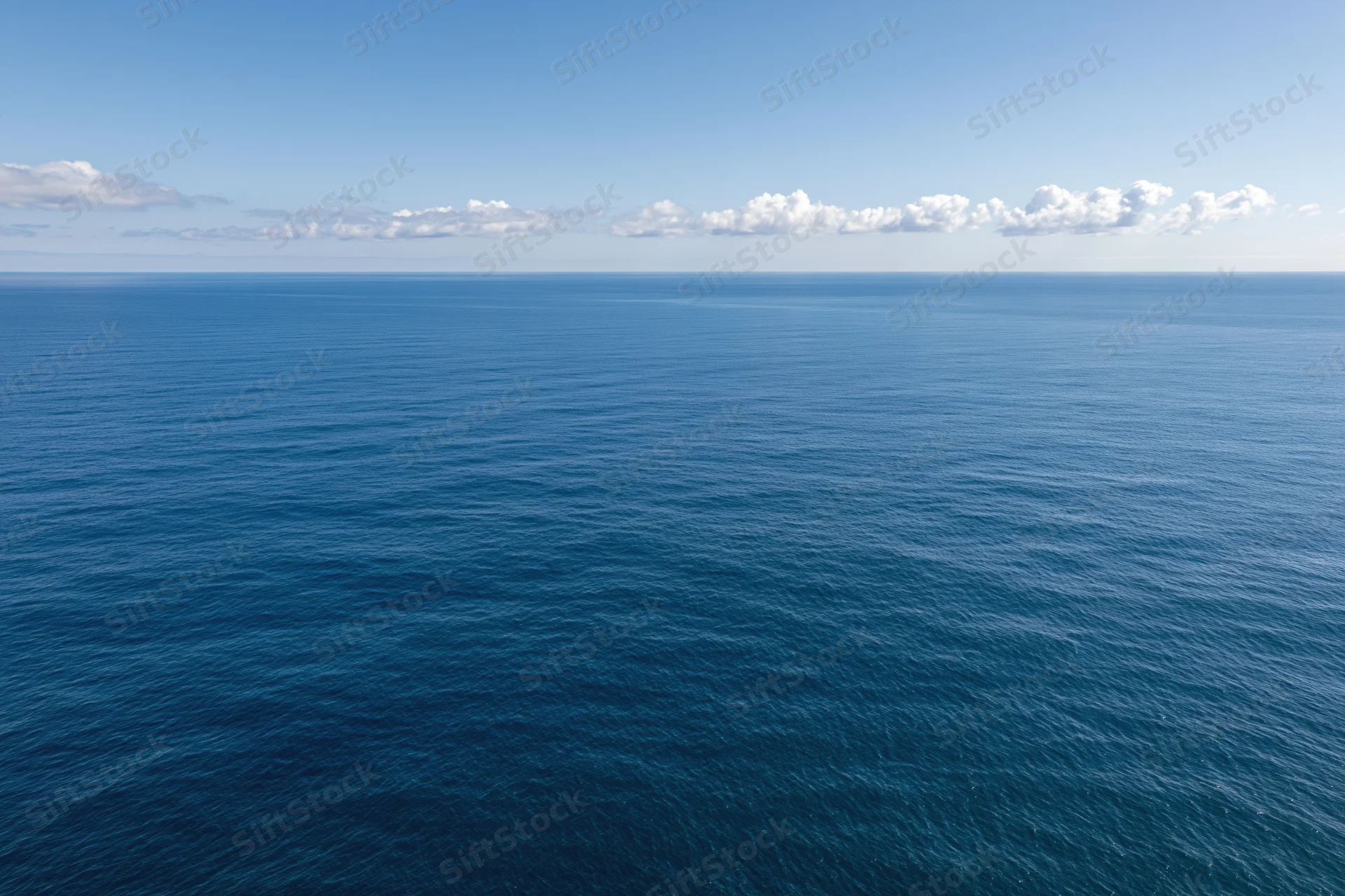 Aerial view of calm open ocean under clear blue sky with scattered clouds along the horizon