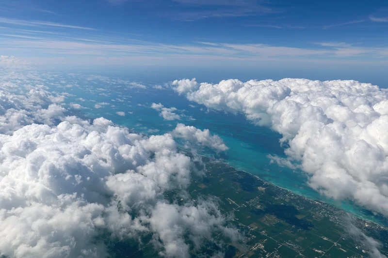 Aerial view of coastline and turquoise ocean from above clouds