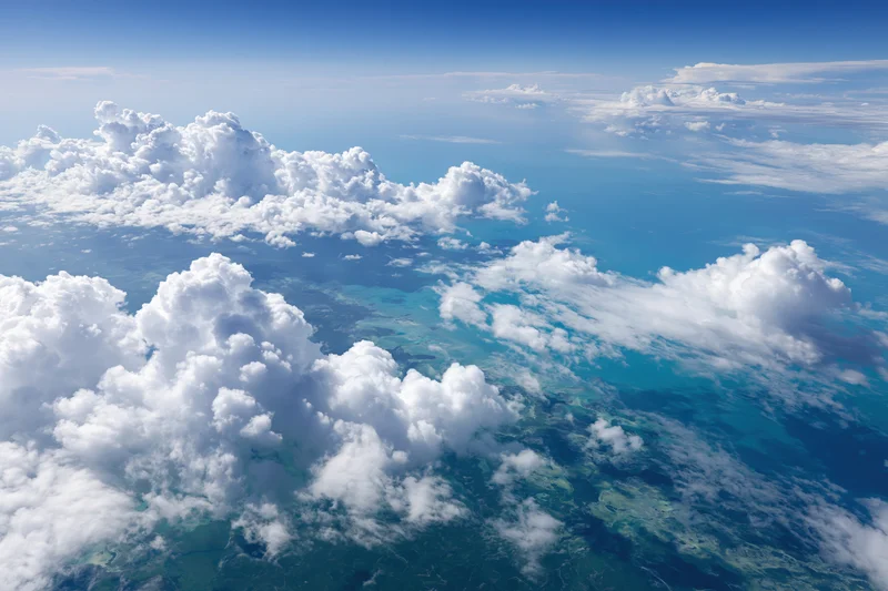 Aerial view of clouds above turquoise ocean and coastline from high altitude