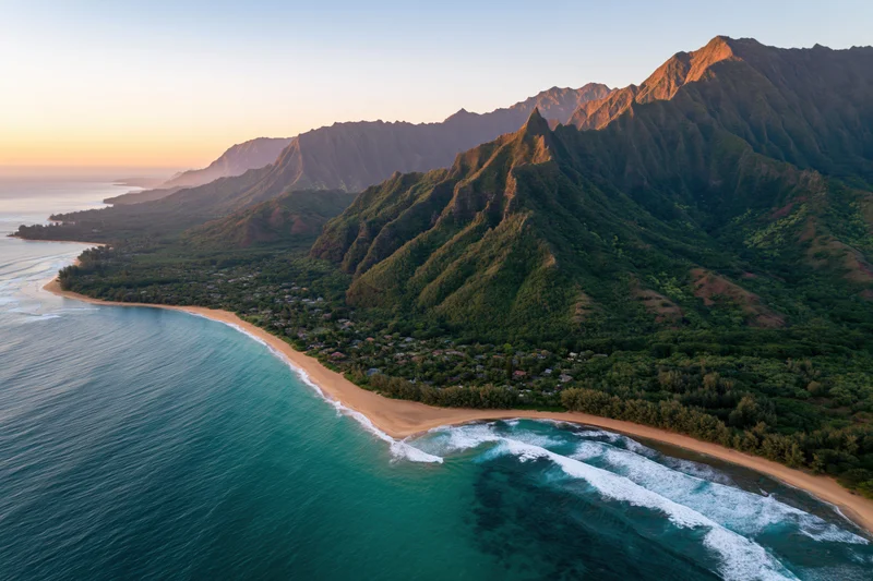 Aerial view of a curved hawaiian beach with golden sand meeting turquoise ocean at sunset